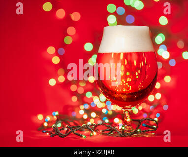 Kurze Glas helles Lagerbier oder Ale mit Weihnachtsbeleuchtung auf rotem Hintergrund Stockfoto