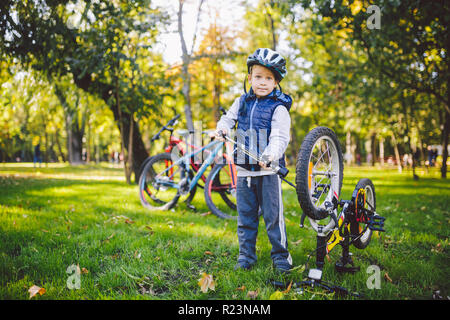 Thema Kind und Beruf. Eine kleine blonde Caucasian boy verwendet ein Fahrrad Pumpe pumpt Luft in einen Reifen Rad Fahrrad, ein Kind Reparaturen ein Fahrrad in einem mir Stockfoto