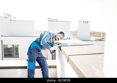 Builder in Uniform die Metallabdeckung an der Brüstung eines neuen Gebäudes Stockfoto