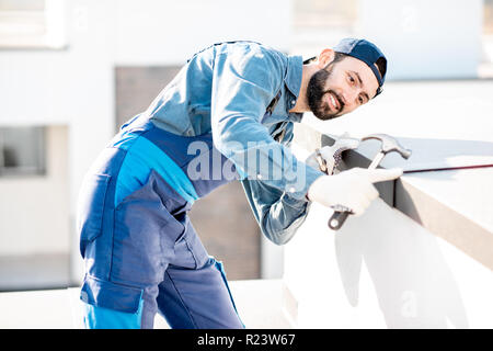 Builder in Uniform die Metallabdeckung an der Brüstung eines neuen Gebäudes Stockfoto