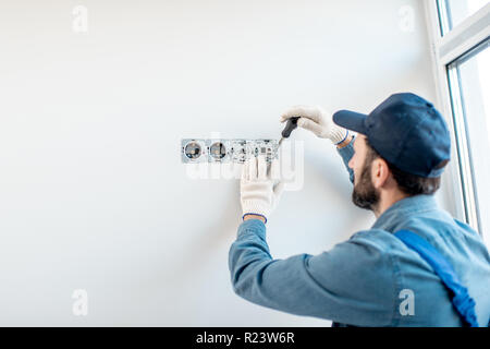 Elektriker in Uniform die Steckdosen auf der weißen Wand im Innenbereich Stockfoto