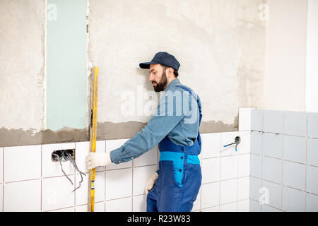 Arbeiter in der blauen Uniform der Ölstand während der Installation von weißen Fliesen im Badezimmer Stockfoto