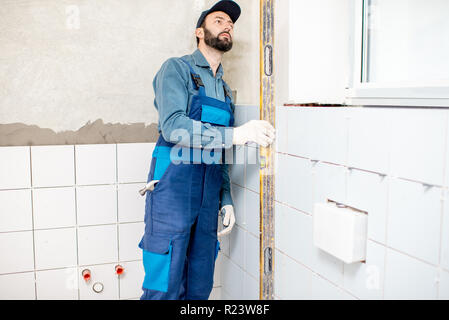 Arbeiter in der blauen Uniform der Ölstand während der Installation von weißen Fliesen im Badezimmer Stockfoto
