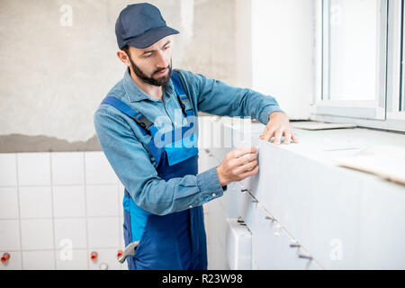 Arbeiter in der blauen Uniform Installation von weißen Fliesen im Badezimmer Stockfoto