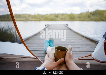 Foto von Frau mit Eisen Becher in die Hände sitzen auf hölzernen Brücke am Fluss Stockfoto