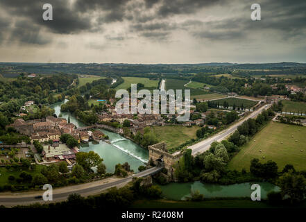 Antenne Panorama der mittelalterlichen befestigten Brücke von Valeggio sul Mincio in der Nähe von Verona mit dem Borghetto und kleinen Wasserfall, grüne Wasser, bewölkter Himmel Stockfoto