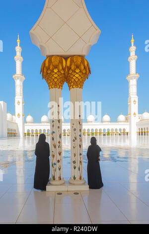 Zwei (2) touristische Frauen tragen traditionelle schwarze Abaya Kleidung bewundern die Schönheit der Sheikh Zayed Moschee in Abu Dhabi, Vereinigte Arabische Emirate. Stockfoto