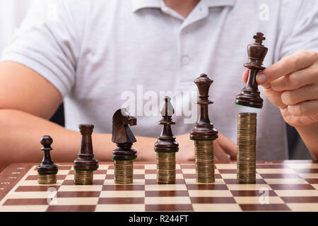 Des Menschen Hand König Schachfigur auf Gestapelte Münzen Schachbrett Stockfoto