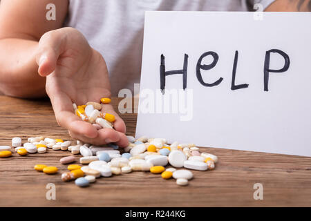 Man's Hand, die Pillen mit Hilfe Text auf Papier über Holz- Schreibtisch Stockfoto