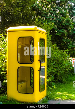 Eine alte helle gelbe Telefonzelle mit abgerundeten Kanten, schwarz-umrandete Fenster und eine schwarze Tür aus der Vergangenheit in Deutschland. Sie verschwanden aus dem... Stockfoto