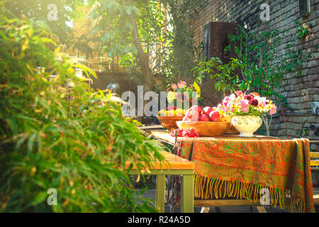 Schön hölzernen Tisch voll von verschiedenen Arten von Früchten in glänzenden schönen Garten mit vielen Blumen und grünes Laub um eingerichtet Stockfoto