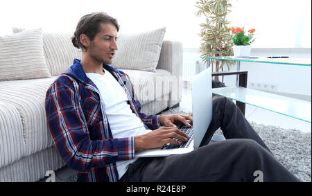 Moderne Kerl mit einem Laptop auf den Boden neben das Sofa Stockfoto