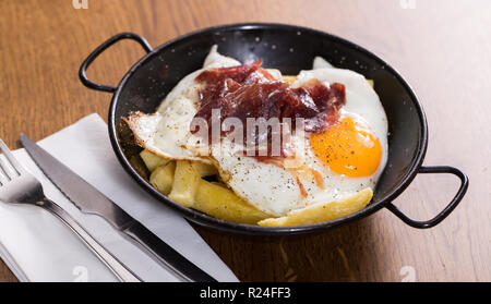 Leckere Eier mit Jabugo Schinken in schwarz Bratpfanne auf hölzernen Tischplatte Stockfoto