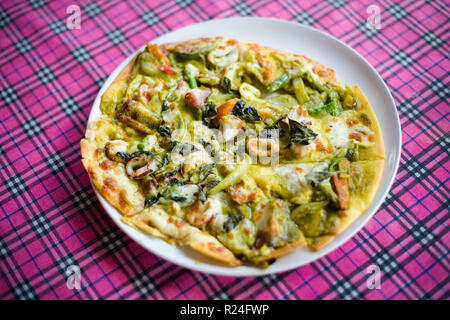 Frisch zubereitete asiatische aromatische grüne Curry Sauce Pizza mit Meeresfrüchten in einem lokalen Restaurant auf Koh Lanta Island. Traditionelle thailändische Küche aus frischen ingredie Stockfoto