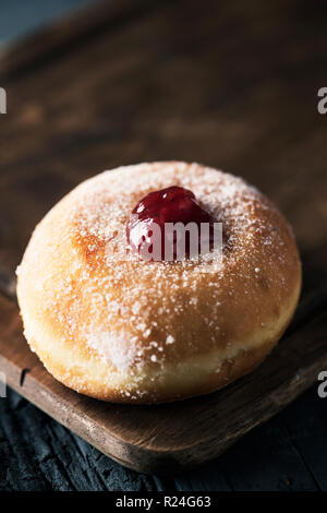 Nahaufnahme eines sufganiyah, eine jüdische Krapfen gefüllt mit Strawberry jelly traditionell gegessen auf Hanukkah, auf einem rustikalen Holztisch Stockfoto