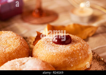 Nahaufnahme von einigen sufganiyot, jüdische Krapfen gefüllt mit Strawberry jelly traditionell gegessen auf Hanukkah, und einige Kerzen auf einem Tisch Stockfoto