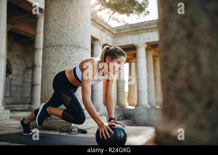 Fitness-Frau macht Liegestütze mit einem Medizinball. Frau in Fitnesskleidung, die mit einem Medizinball trainiert. Stockfoto