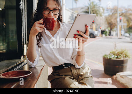 Frau, die eine Brille im Café trägt, mit einem digitalen Tablet, das Kaffee trinkt. Geschäftsfrau trinkt Kaffee im Café. Stockfoto