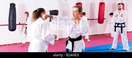 Porträt der sportliche junge Kinder in paar Beherrschung neuer Karate bewegt sich während der Gruppe Klasse mit männlichen Trainer Stockfoto