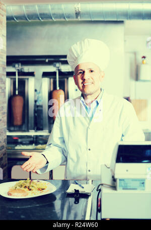 Reife männliche Chef tragen einheitliche Halteplatte mit frisch zubereiteten Kebab und Gemüse im Restaurant Stockfoto