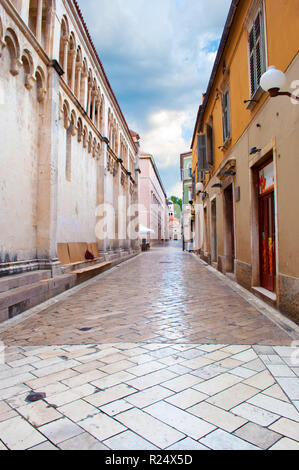 Gemütliche und leere Gasse zwischen zwei Häusern aus Stein an einem Sommermorgen. Dramatische Wolkenhimmel. Zadar, Kroatien Stockfoto