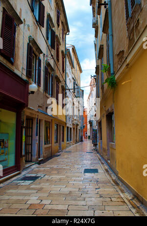 Gemütliche und leere Gasse zwischen zwei Häusern aus Stein mit Türen und Fensterläden an einem Sommermorgen. Zadar, Kroatien Stockfoto