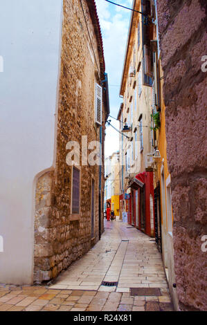 Gemütliche und leere Gasse zwischen zwei Häusern aus Stein mit Fensterläden an einem Sommermorgen. Zadar, Kroatien Stockfoto