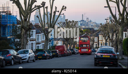 London, England, Großbritannien - 20 April 2015: Die Docklands skyline steigt hinter der traditionellen suburban Reihenhäuser und Verkehr auf einem Hügel Straße zwischen Stockfoto