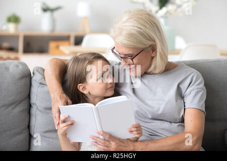 Liebevolle Großmutter lehre Enkelin lesen Buch sitzen o Stockfoto