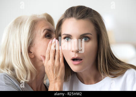 Ältere Mutter Flüstern in jungen Tochter Ohr sagen schockierend n Stockfoto