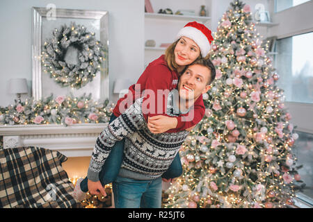 Schönes und positives Bild der jungen Paare in eine Richtung suchen. Sie umarmt ihn. Mann hält Frau. Sie ist auf seinem Rücken. Paar in dekoriert Ro Stockfoto