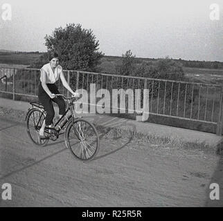 1960 s, attraktive junge Frau mit dem Fahrrad auf den Weg über die Brücke in die Landschaft. Stockfoto