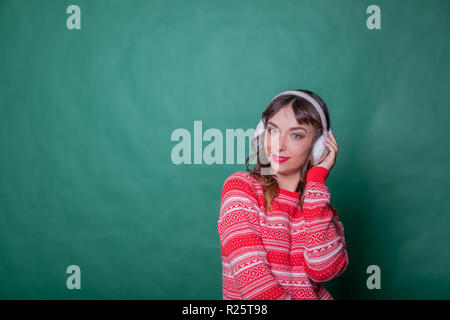 Winter Schönheit Frau auf der grünen Wand Hintergrund. Winterurlaub Konzept. Haut- und Haarpflege in der kalten Jahreszeit. Schöne Frau mit langem Haar zu tragen Pullover und Ohrenschützer. Platz kopieren Stockfoto