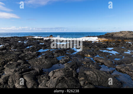 Schwarze Vulkangestein auf westlichen Hawaiian Beach in der Nähe von Kona. Tidepools unter den Felsen, Wellen und den Pazifischen Ozean in der Ferne. Stockfoto