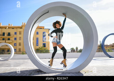 Junge passen schwarze Frau auf Rollschuhen reiten im Freien auf Urban Street. Lächelnde Mädchen mit Afro Frisur rollerblading an einem sonnigen Tag Stockfoto