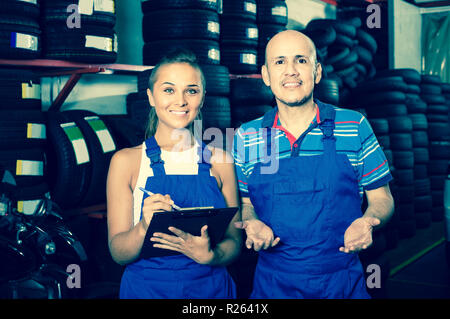 Junge positive weibliche Techniker in Overalls holding Zwischenablage in Kfz-werkstatt Stockfoto