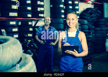 Junge Frau in Uniform stehen und schreiben Sie die Daten in auto Werkstatt Stockfoto