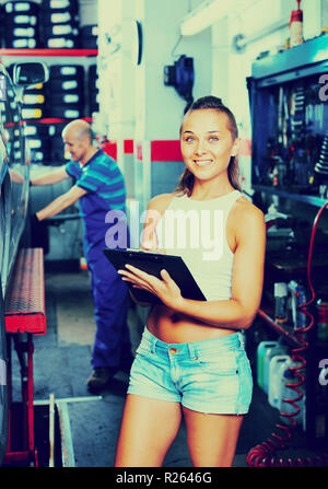 Junge lächelnde froh, Frau stehen und schreiben Sie die Daten in dem Auto Service Stockfoto