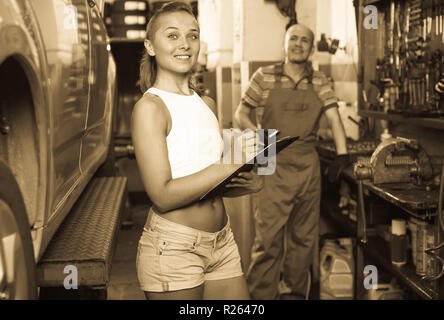 Junge lächelnde fröhliche Frau stehen und schreiben Sie die Daten in dem Auto Service Stockfoto