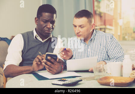 Zwei gestörten Freunde per Telefon in den Händen diskutieren Papiere, während zu Hause sitzen Tabelle Stockfoto