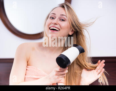 Portrait der junge lächelnde Mädchen ihre Haare trocknen mit Haartrockner im Schlafzimmer Stockfoto