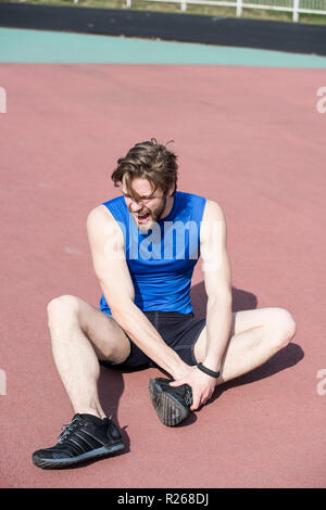 Verletzten Läufer, bärtiger Mann oder Mann mit athletischen Körper auf der Laufstrecke Gefühl Schmerz der gebrochenen Bein sonnige in blau Sportbekleidung. Sommer Aktivität, Sport. gesunder Lebensstil und Workout. sport Trauma Stockfoto