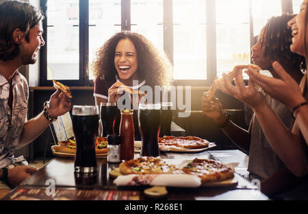 Junge Frau essen Pizza und Lachen beim Sitzen mit Ihren Freunden in einem Restaurant. Eine Gruppe von Freunden zu genießen, während Sie das Essen und die Getränke im Café. Stockfoto