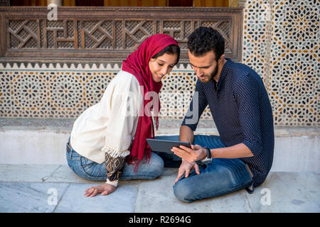 Junge muslimische Paare in Beziehung Lächeln während der Arbeit auf dem Tablet im traditionellen arabischen Ambient Stockfoto