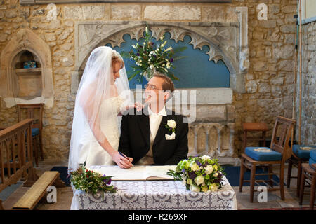 Braut und Bräutigam lächelnd an, da Sie das Register in der Kirche anmelden Stockfoto