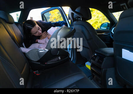 Mutter an ihr Kind im Kindersitz auf dem Rücksitz des Autos mit schwarzen Interieur suchen, erreichen durch die offene Tür, Schuß von der Seite mit Kopieren s Stockfoto