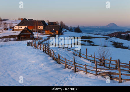 Herrliche Winterlandschaft. Winter Sonnenuntergang, alte ländliche Mountain Chalets aus Holz und verschneiten Hügeln in der Nähe von Brasov, Siebenbürgen, Rumänien Stockfoto