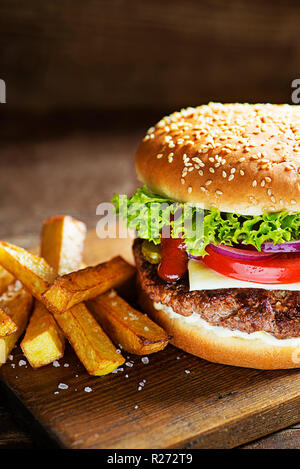 Lecker Hamburger mit Käse und Pommes frites auf Holztisch und dunklen Hintergrund Stockfoto