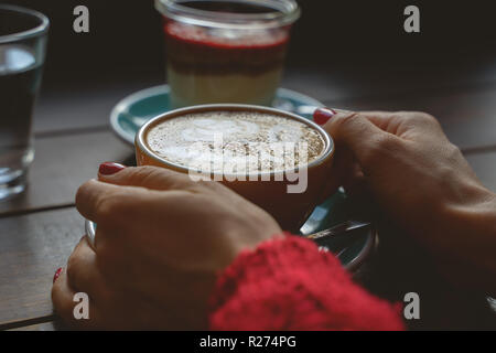 Weibliche Hände halten eine Tasse Kaffee ein Dessert auf hölzernen Tisch Stockfoto