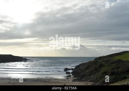 Blick auf eine kleine Bucht auf der schönen Insel Anglesey in Nordwales. Dämmerung, und Sonnenlicht reflektiert über die sanften Wellen brechen auf dem Sand. Stockfoto